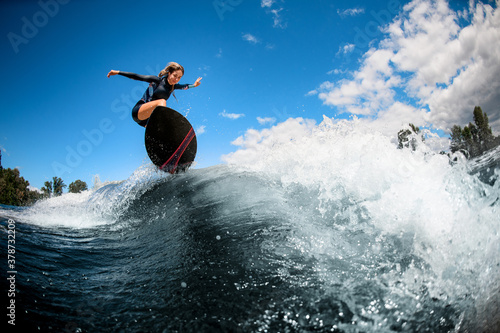 Photography view of young energetic woman on surfboard jumping over the wave