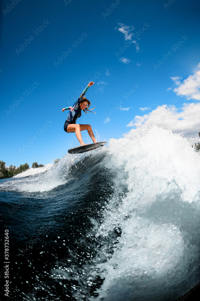 cheerful young woman skillfully jumping with surf board on wave