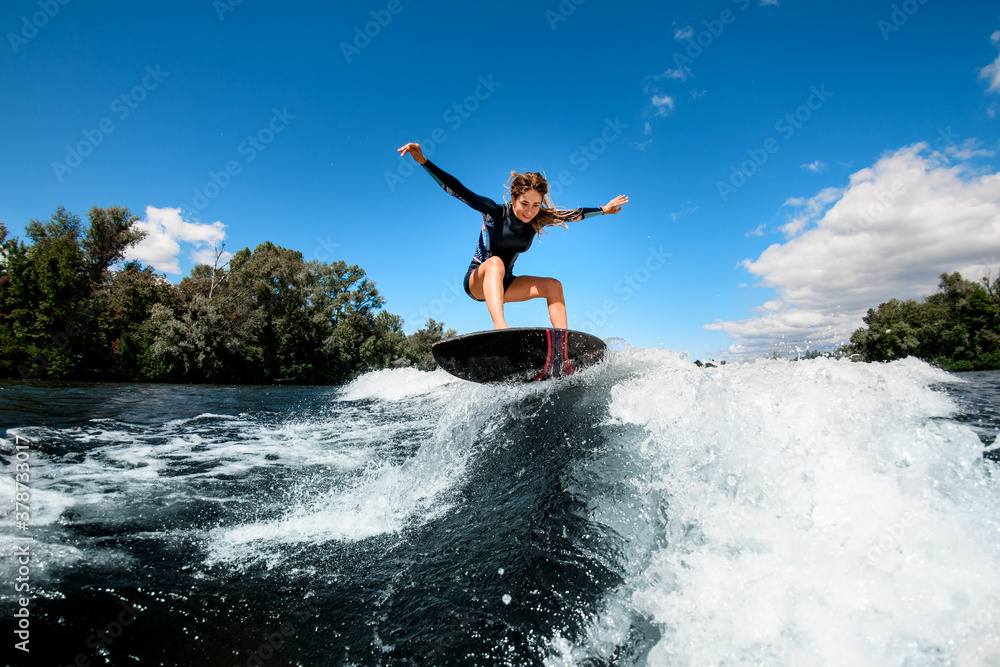 active woman coolly balancing on surfboard on splashing wave