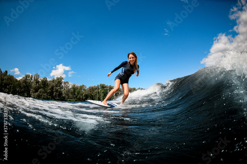 Cheerful pretty young woman in swimsuit rides down the wave on surfboard
