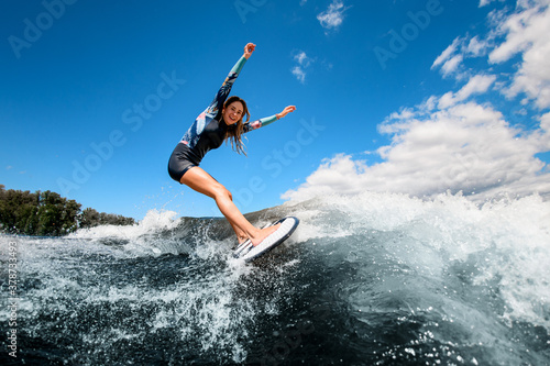 Active cheerful woman in swimsuit vigorously ride the wave on surfboard