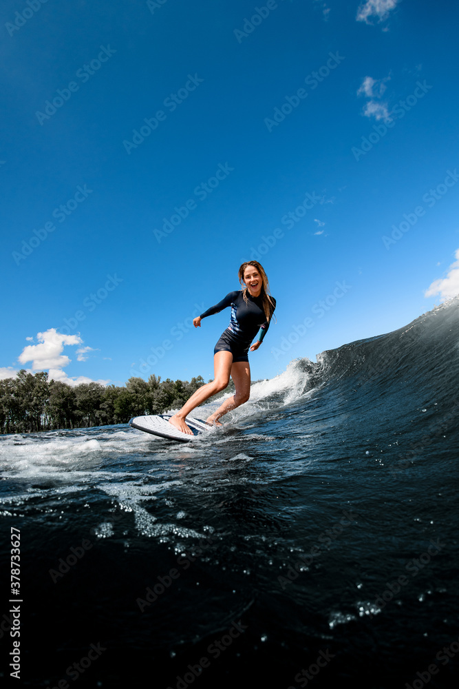 happy young woman in swimsuit rides down the wave on surfboard