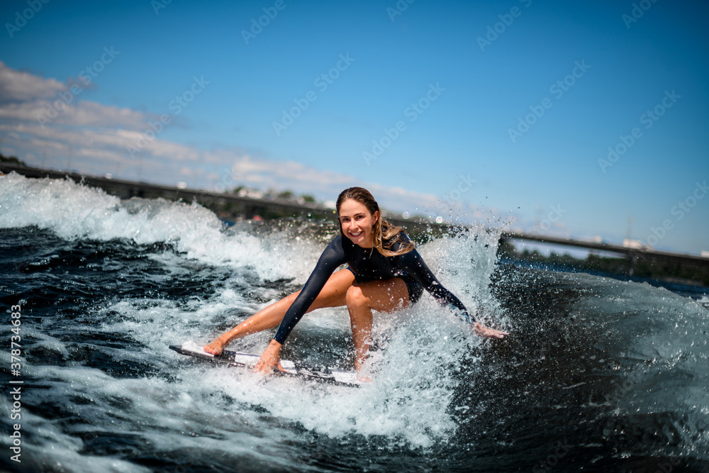 view of girl having fun sitting on surf board and touching the water with her hand.