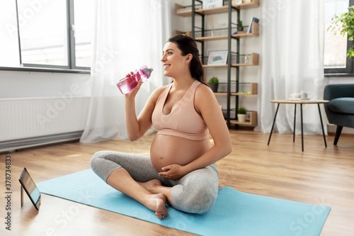 sport, fitness and people concept - happy smiling pregnant woman drinking water after yoga at home