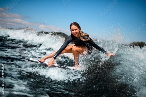 smiling girl having fun sitting on surf board and touching the water with her hand.