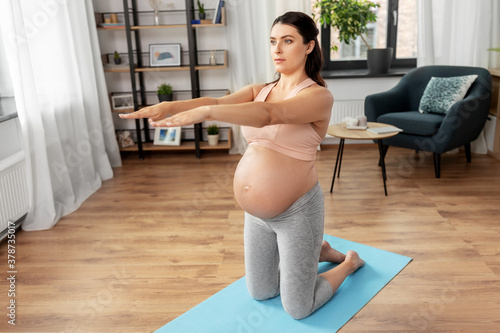 sport, fitness and pregnancy concept - happy pregnant woman exercising at home