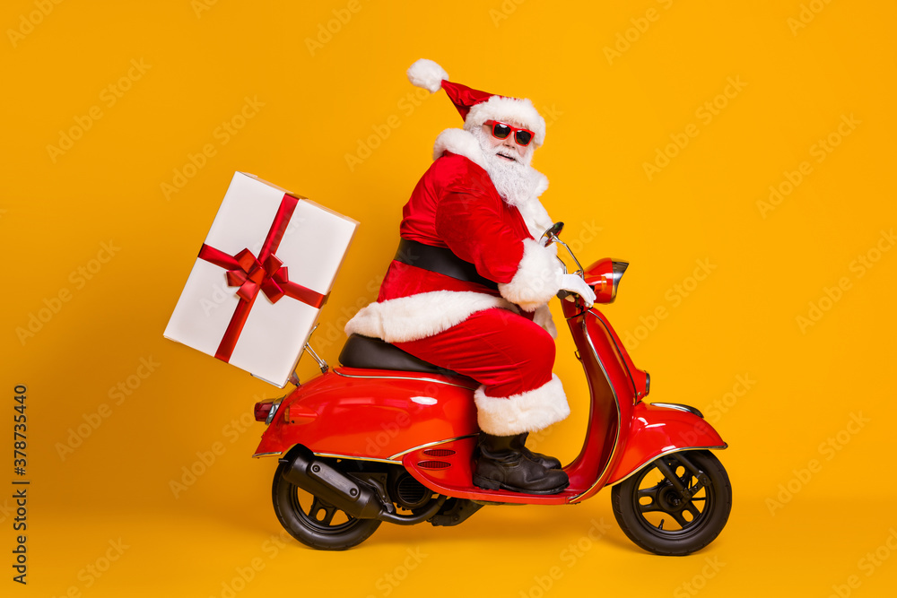 Full length profile side photo of grey white hair bearded santa claus ride drive bike deliver gift box x-mas christmas night wear red headwear isolated yellow color background Full length profile side photo of grey white hair bearded santa claus ride drive bike deliver gift box x-mas christmas night wear red headwear isolated yellow color background