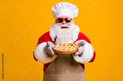 Photo of cheerful santa claus chef headwear grandpa grey beard hold fresh sweet big pie jam filler wear red x-mas costume gloves sun specs cap apron isolated yellow color background