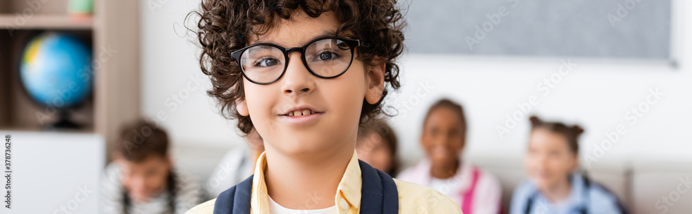 Panoramic shot of muslim schoolboy looking at camera in classroom Panoramic shot of muslim schoolboy looking at camera in classroom