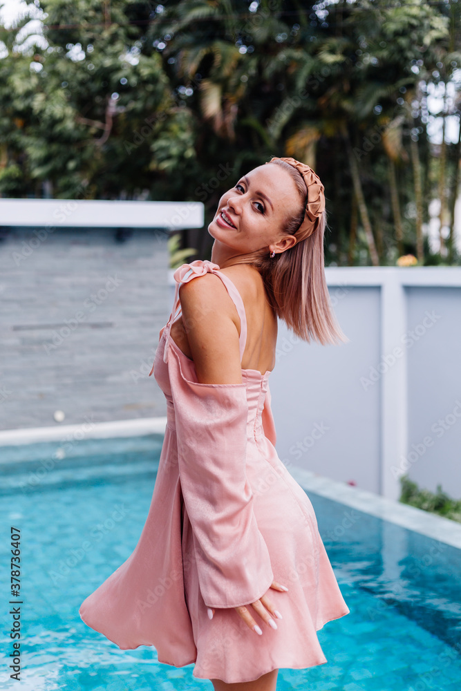 Happy caucasian calm stylish cute woman in pink summer dress and elegant brown headband standing on teracce at villa enjoying beautiful day alone. Happy caucasian calm stylish cute woman in pink summer dress and elegant brown headband standing on teracce at villa enjoying beautiful day alone.