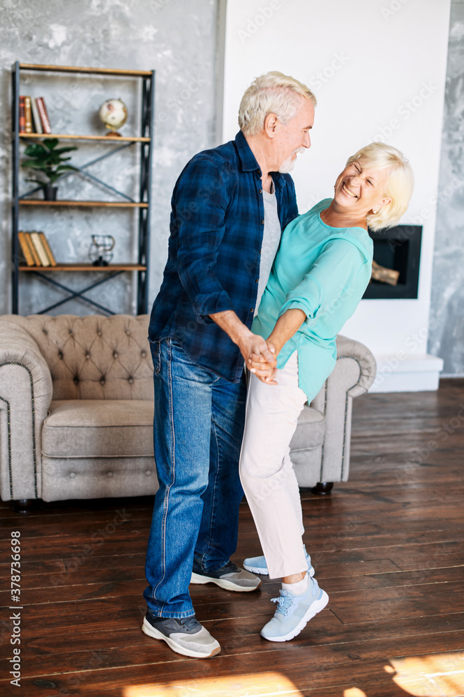 Joyful elderly couple has fun in the cozy living room. A happy senior wife and husband are dancing a tango at home. Joyful elderly couple has fun in the cozy living room. A happy senior wife and husband are dancing a tango at home.