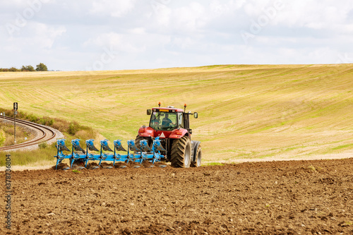 Farmer in a big red tractor preparing land with plow for sowing