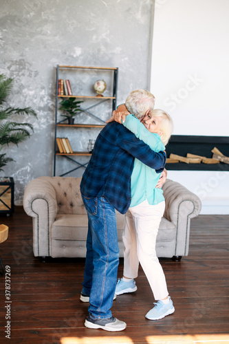 Portrait of modern romantic elderly couple is hugging, embracing gently, dancing at home. Senior spouses holding each other in arms and laugh happily © Vadim Pastuh