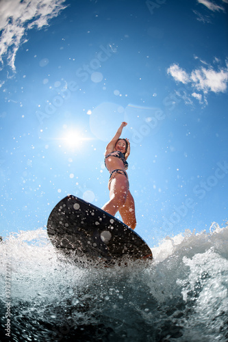 Close-up of surfboard on which woman standing and riding on splash wave.
