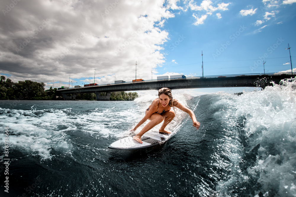 Naklejka premium Active girl having fun sitting on surf board and touching the water with her hand.