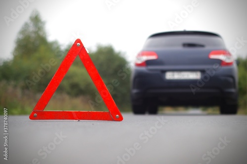 Accident on the road. Emergency warning triangle near damaged broken car. Automobile needs service