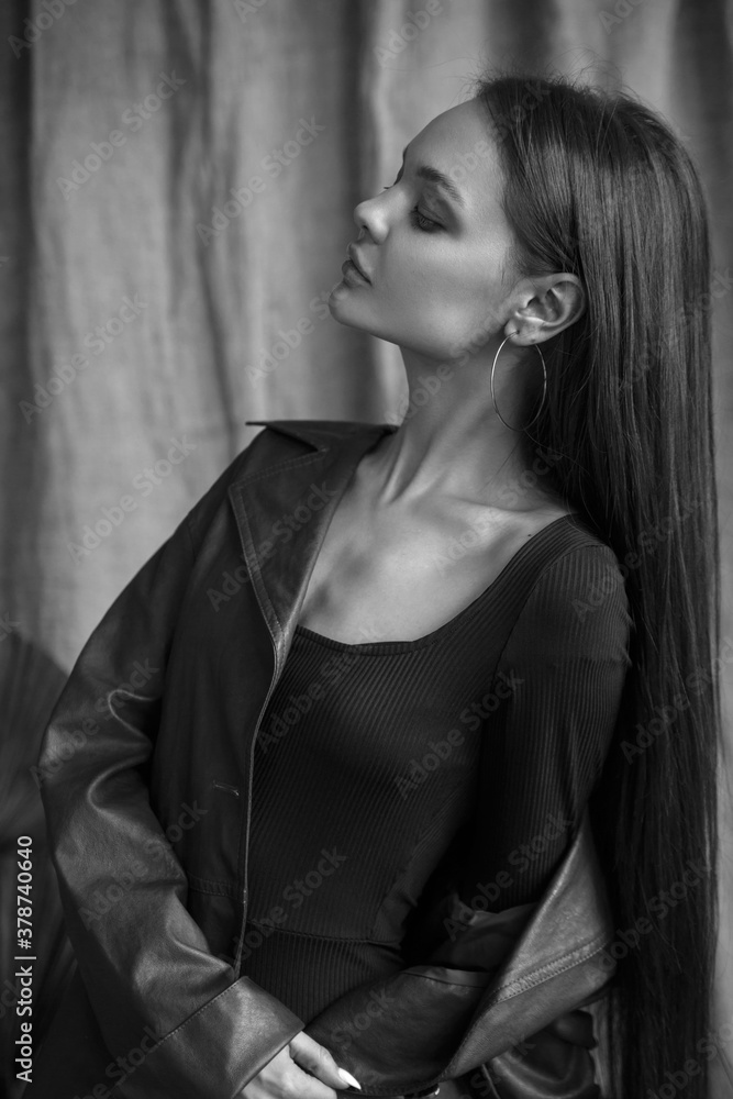 Black and white fashion portrait of a beautiful girl with natural makeup in a leather coat in the studio.
