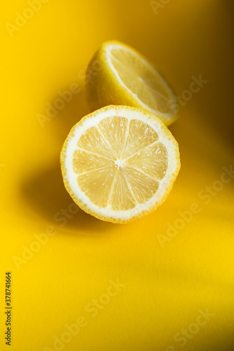 Half of ripe fresh lemon citrus with sun and shadows on yellow background. Vertical image.