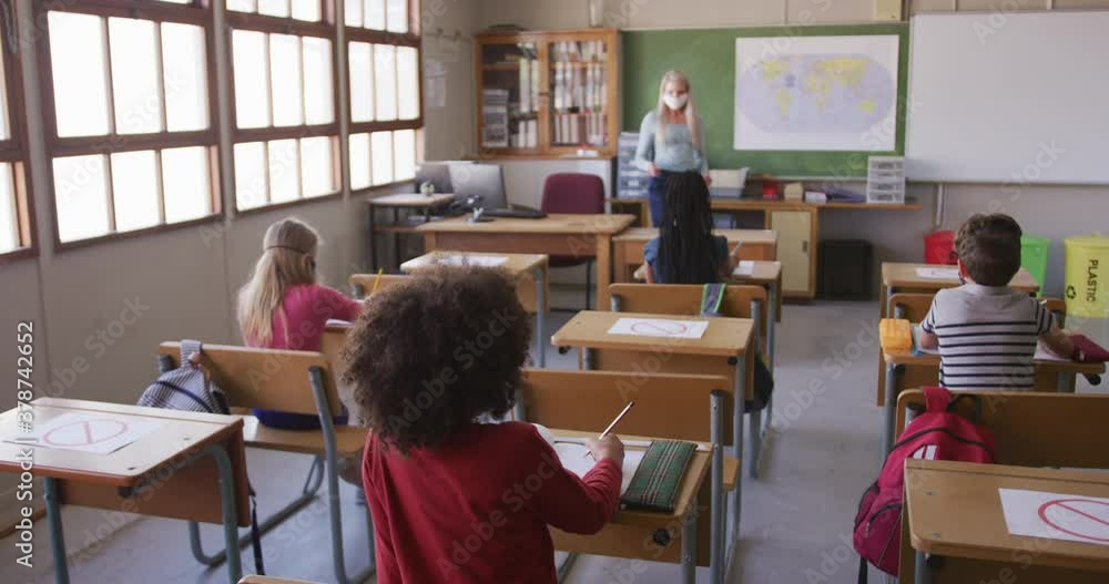 Group of kids wearing face mask raising their hands in the class at school Group of kids wearing face mask raising their hands in the class at school