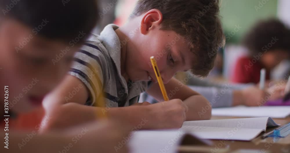 Two boys writing while sitting on their desk at school Two boys writing while sitting on their desk at school