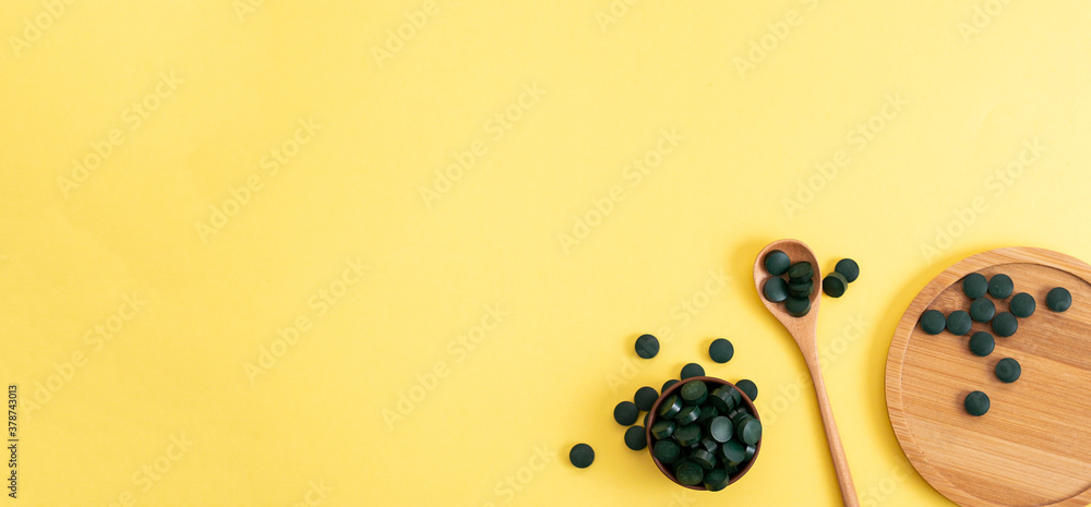 spirulina in tablets with wood spoon and jar on yellow background. Concept natural, eco, powder healthy dietary supplement. Copyspace, banner spirulina in tablets with wood spoon and jar on yellow background. Concept natural, eco, powder healthy dietary supplement. Copyspace, banner