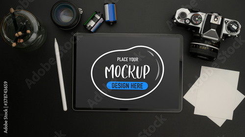 Mock up digital tablet on black table with camera, notepad, lens and stationery