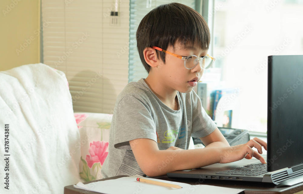On Asian boy student is learning online class and studying by video call. The happy boy learns english language with laptop at home.New normal.Covid-19 coronavirus, social distancing and staying home. On Asian boy student is learning online class and studying by video call. The happy boy learns english language with laptop at home.New normal.Covid-19 coronavirus, social distancing and staying home.