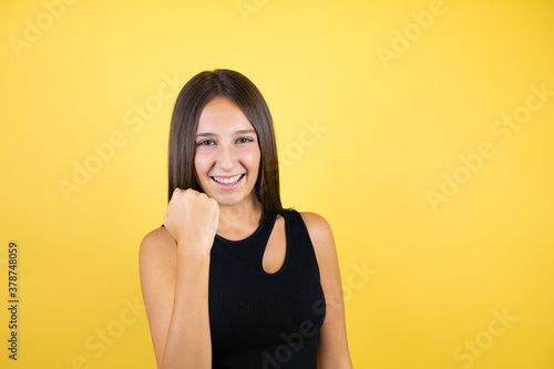 Beautiful young girl kid over isolated yellow background angry and mad raising fist frustrated and furious while shouting with anger. Rage and aggressive concept.