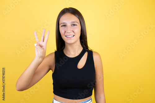 Beautiful young girl kid over isolated yellow background showing and pointing up with fingers number three while smiling confident and happy