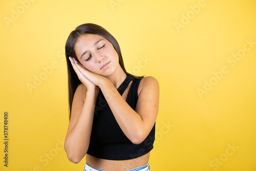 Beautiful young girl kid over isolated yellow background sleeping tired dreaming and posing with hands together while smiling with closed eyes.