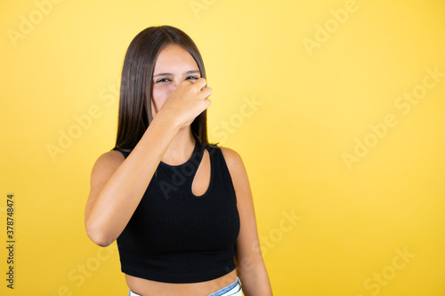 Beautiful young girl kid over isolated yellow background smelling something stinky and disgusting, intolerable smell, holding breath with fingers on nose