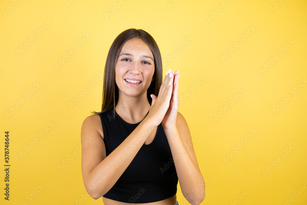 Naklejka premium Beautiful young girl kid over isolated yellow background clapping and applauding happy and joyful, smiling proud hands together