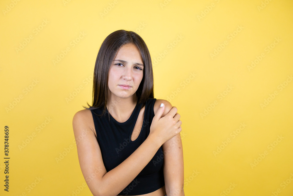 Beautiful young girl kid over isolated yellow background with pain on her shoulder and a painful expression Beautiful young girl kid over isolated yellow background with pain on her shoulder and a painful expression