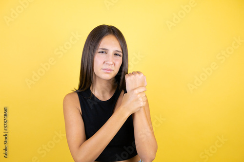 Beautiful young girl kid over isolated yellow background suffering pain on hands and fingers, arthritis inflammation