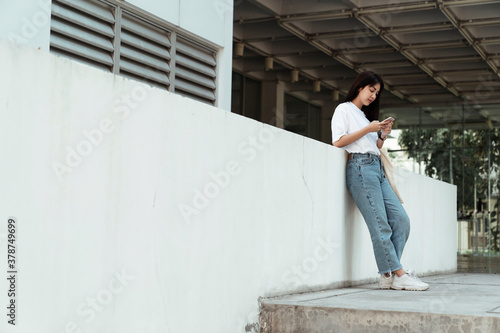 University student leaning on wall using smartphone.