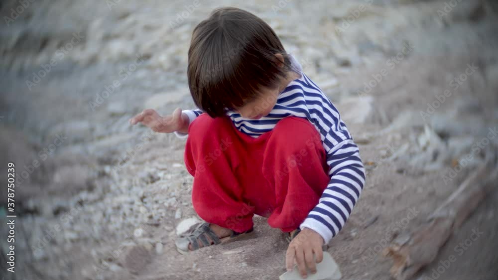 boy child in a blue vest dripping sand with a stone on the beach by the sea in summer boy child in a blue vest dripping sand with a stone on the beach by the sea in summer