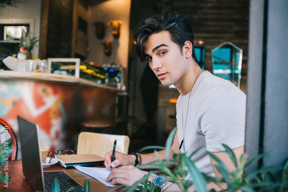 Freelancer taking notes using laptop while sitting at cafe