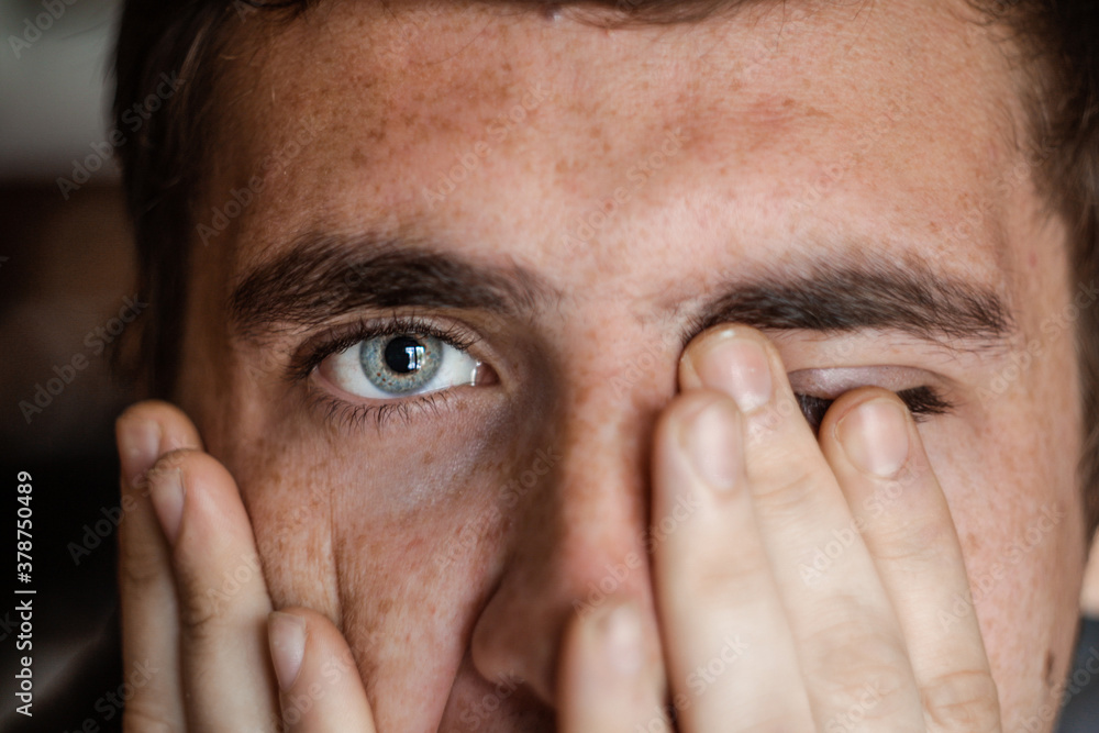 The young European brunet guy covered his face with his hands. Tired and desperate person. Blue-gray eyes and freckles on the face. Basic emotions of sadness. Close-up. Selective focus. The young European brunet guy covered his face with his hands. Tired and desperate person. Blue-gray eyes and freckles on the face. Basic emotions of sadness. Close-up. Selective focus.