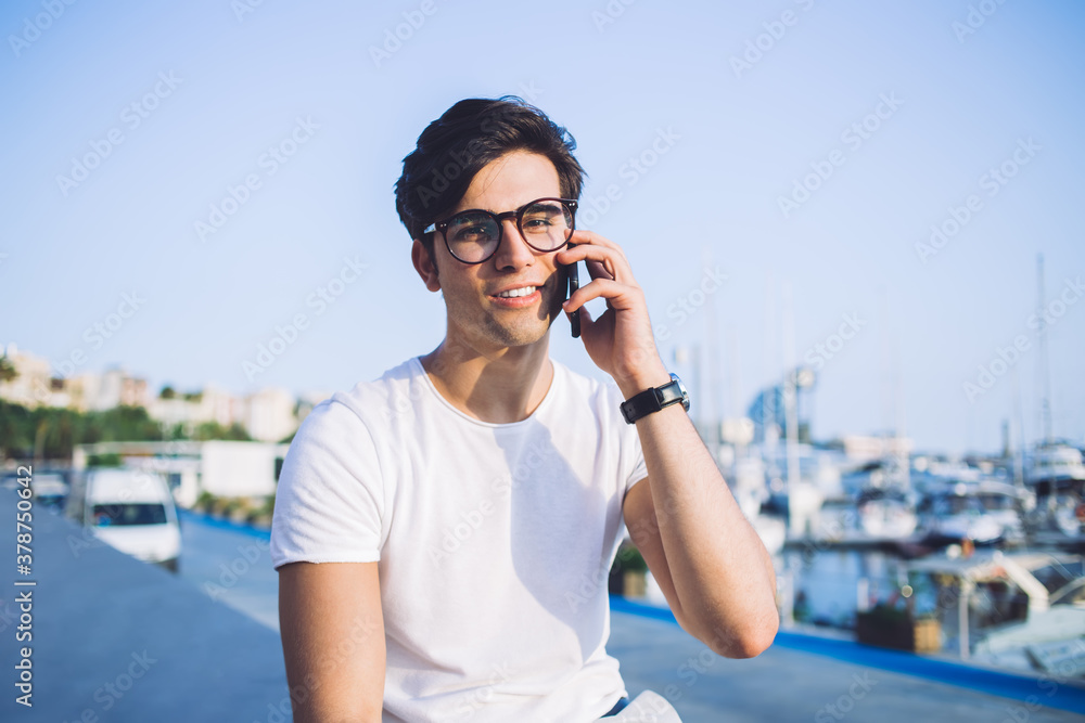 Portrait of cheerful caucasian male tourist in eyewear spending weekends outdoors making smartphone call in roaming, handsome hipster guy in eyewear looking at camera talking on mobile phone Portrait of cheerful caucasian male tourist in eyewear spending weekends outdoors making smartphone call in roaming, handsome hipster guy in eyewear looking at camera talking on mobile phone