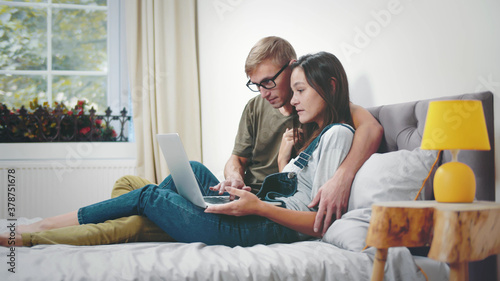 Happy young couple lying on bed using laptop computer at home © nimito