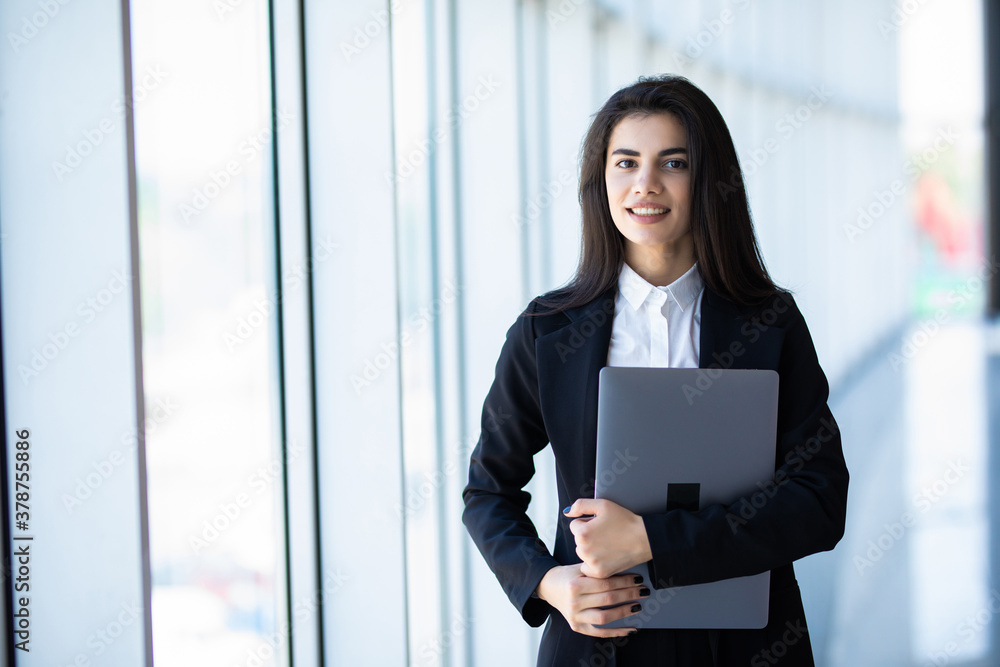 Businesswoman standing in hall with laptop in modern office building Businesswoman standing in hall with laptop in modern office building