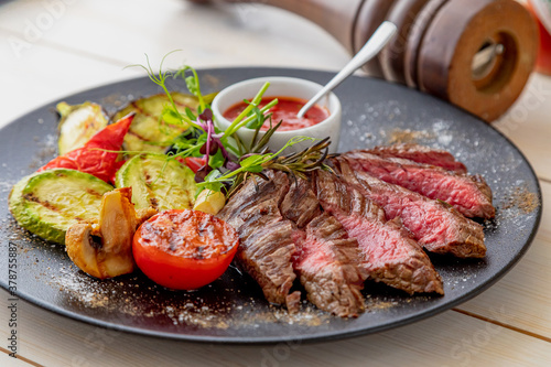chopped medium rare steak with grilled vegetables. Sauce is served with the dish. Dish on a white plate in natural light.
