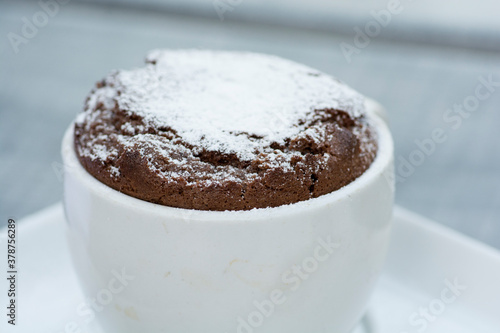 A traditional french dessert - "soufflé", hot chocolate cake, served in a cup, covered with sugar powder.