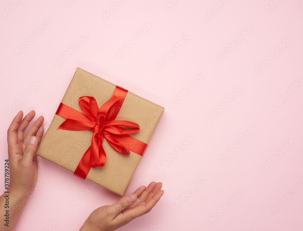 two female hands hold a square box wrapped in brown paper two female hands hold a square box wrapped in brown paper