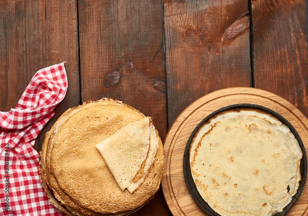 baked round thin pancakes lie stacked on a wooden board, brown table baked round thin pancakes lie stacked on a wooden board, brown table