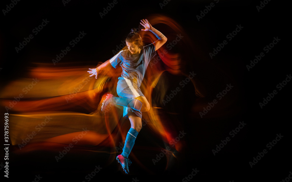 Motion. Football or soccer player on black studio background in mixed light. Young male sportive model training in action. Kicking ball, attacking, catching. Concept of sport, competition, winning.