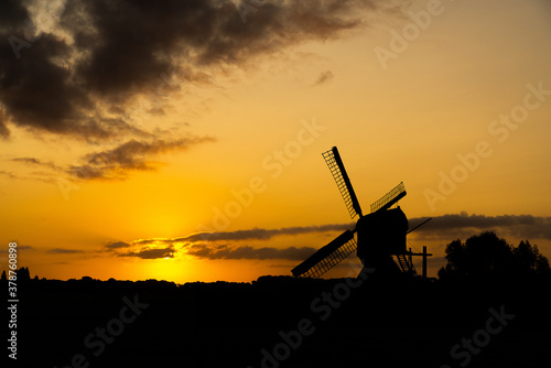 Silhouette of a traditional Dutch windmill against the red orange light of the rising or setting sun