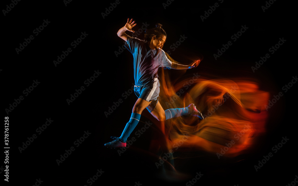 Jump high. Football or soccer player on black studio background in mixed light. Young male sportive model training in action. Kicking ball, attacking, catching. Concept of sport, competition, winning.