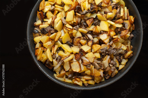 Fried young potatoes with mushrooms and onions. View from above. In a skillet. On a black background.