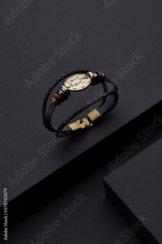 Detailed shot of multilayer leather bracelet with metal charms and metal disc with zodiac sign Libra. The stylish zodiac bracelet with toggle fastener is located on the black matte surface.